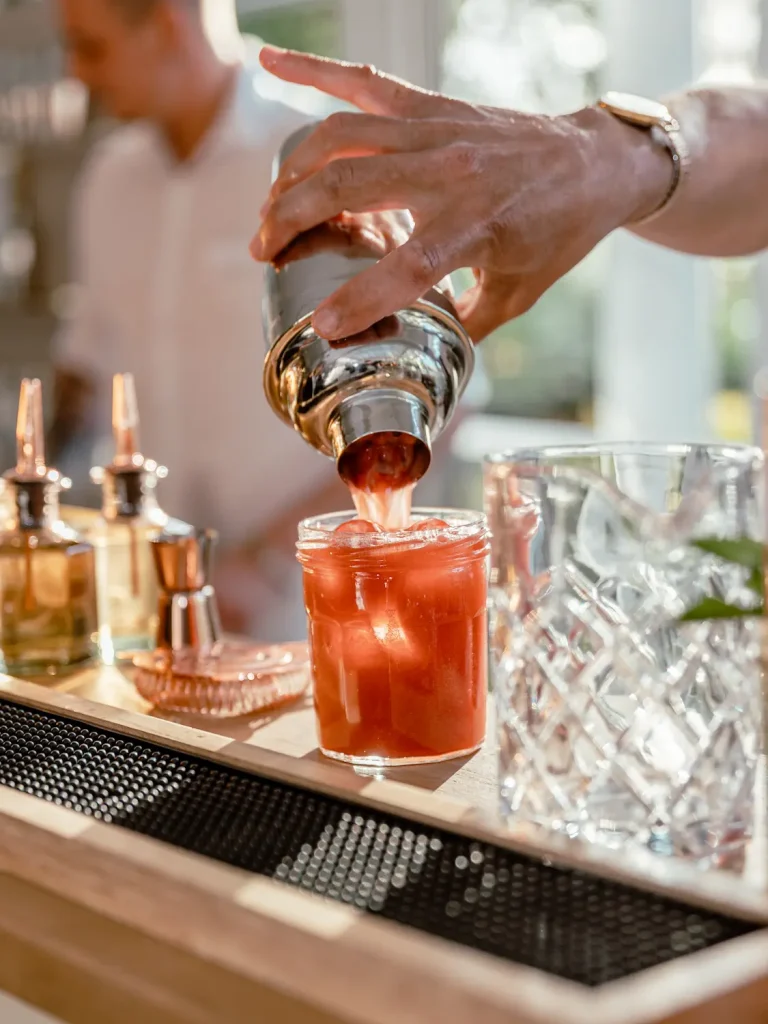 Gros plan sur une main tenant un shaker versant une boisson dans un verre à cokctail
